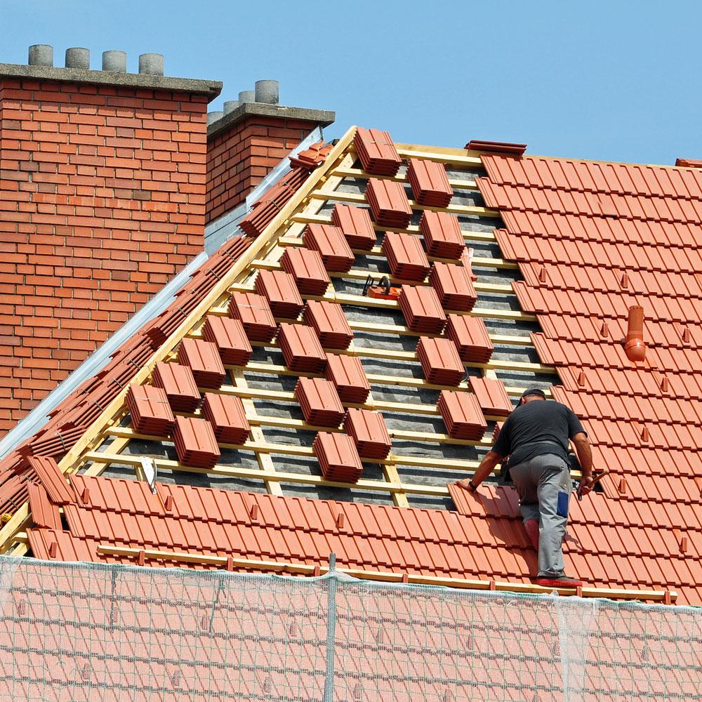 Roofer installing red tiles on a pitched roof with exposed battens
