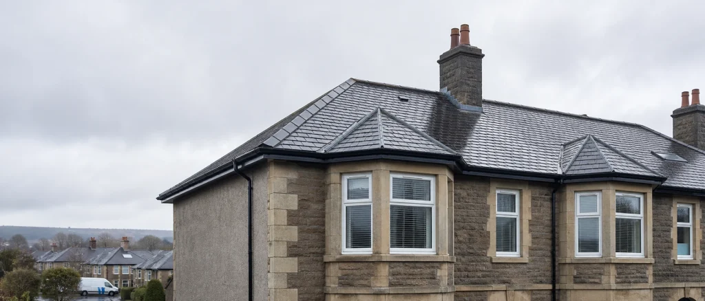 Rain-damp UK home roof with chimney flashing and a slipped tile.