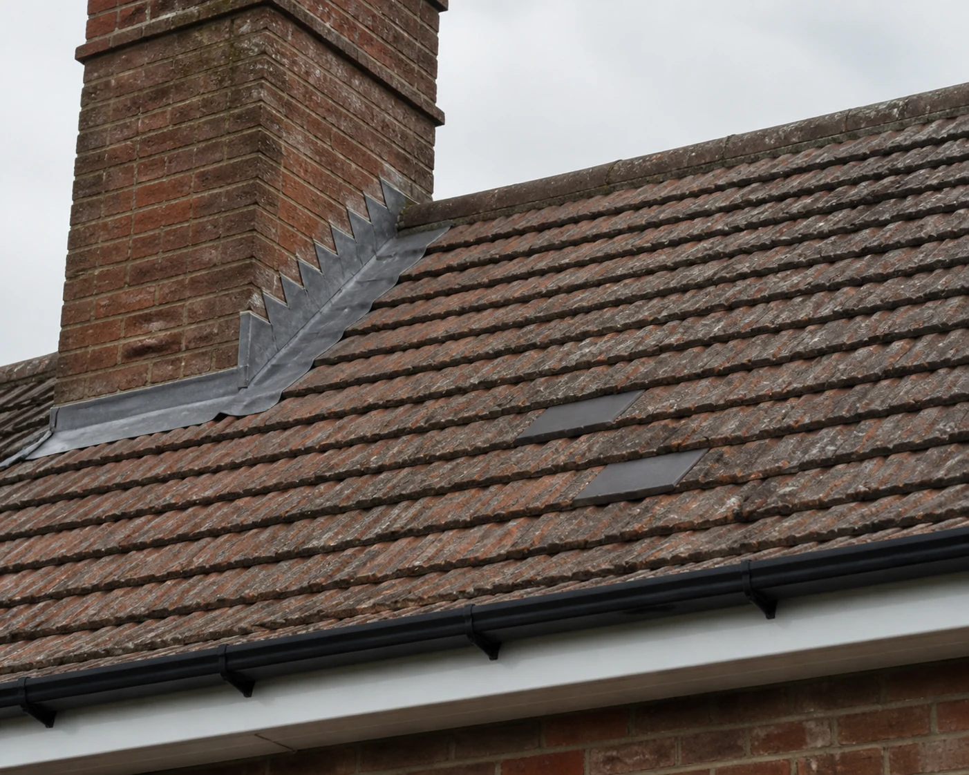 Tiled roof section with chimney flashing, gutter edge and replacement tiles.